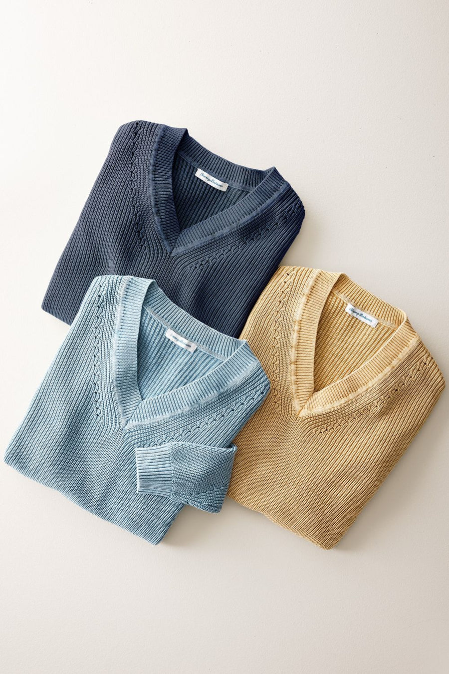 Three Tommy Bahama folded sweaters in blue, green, and beige on a light background