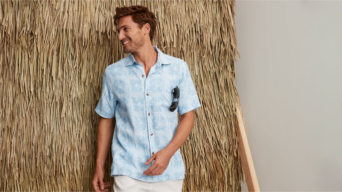 Man wearing a light blue shirt standing in front of a thatched wall.